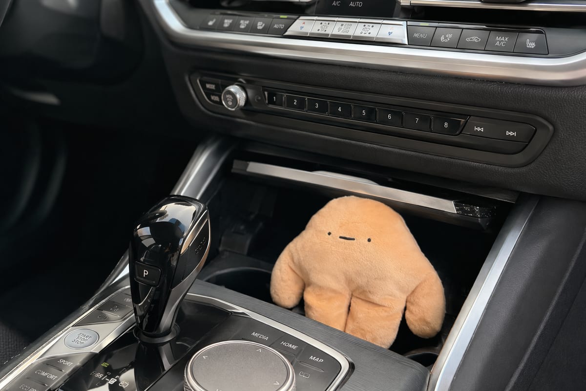An orange pipyaka plush riding along in a car, perched on the center console between the front seats.